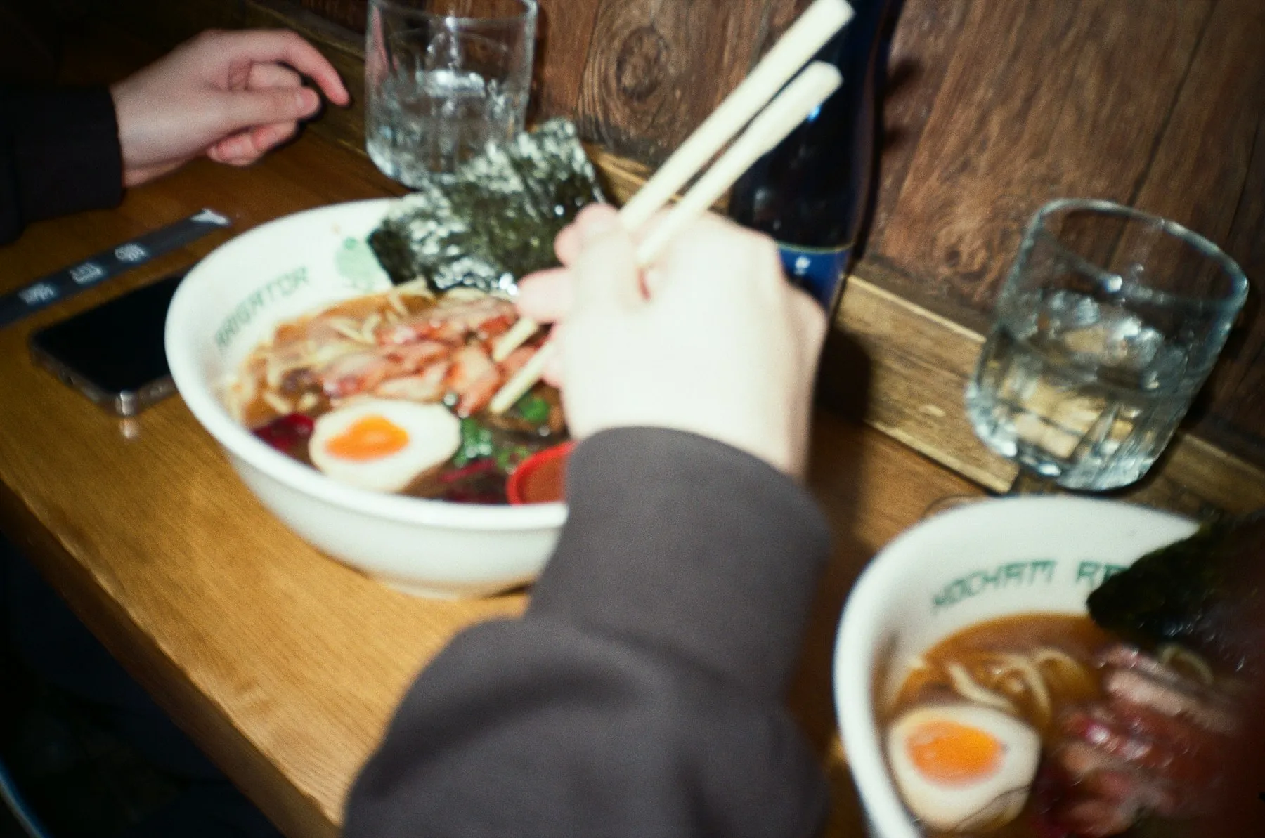 Gäste essen Ramen mit Stäbchen an einem Holztisch